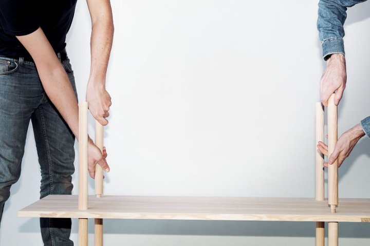 Je zwei Arme schrauben die Zwischenstäbe an den Enden eines Tablars zu einem Holzregal zusammen.