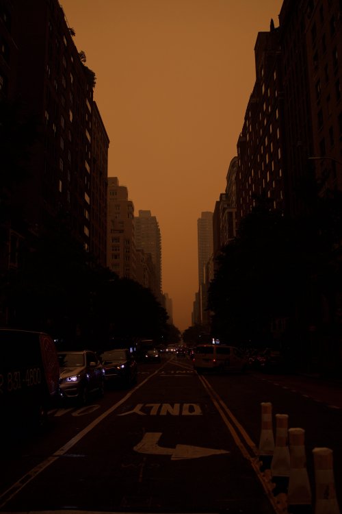 Aufnahme einer Strasse in New York mit Wolkenkratzern links und rechts bei orange-rotem Himmel.