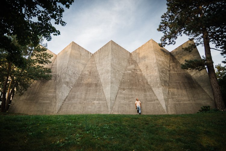 Aussenansicht eines markanten Schulgebäudes mit einem markant gefalteten Betondach, dessen scharfe Kanten und Winkel an ein aufgefaltetes Origami erinnern.