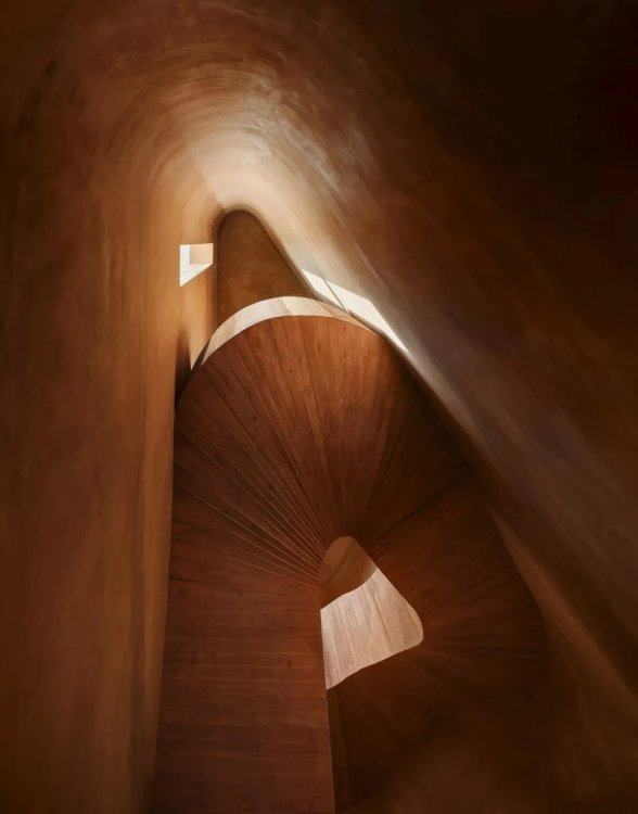Blick von unten eines spiralförmigen Treppenhauses mit geschwungenen Wänden und Licht, das von oben durch Öffnungen einfällt.